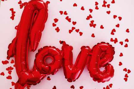 Love flat lay. Happy valentines day. Stylish love word balloon and red hearts confetti on pink background. Love backgroundの写真素材