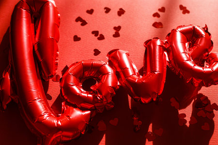 Love flat lay. Happy valentines day. Stylish love word balloon and red hearts confetti on red background. Love backgroundの写真素材