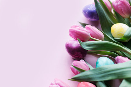 Happy Easter! Colorful easter eggs with pink tulips flat lay border on pink background, space for...