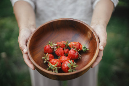 Woman holding wooden bowl with strawberries close up. Gathering fresh natural berries in urban organic garden. Homestead lifestyleの写真素材