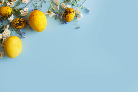 Happy Easter! Modern yellow eggs and spring blossom flat lay with space for text on blue background....