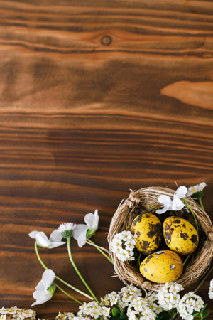 Happy Easter! Modern yellow easter eggs in nest and white spring flowers flat lay with space for text on rustic wooden background. Easter bannerの写真素材