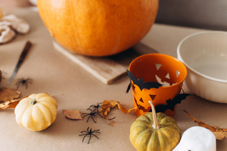Happy Halloween. Carving halloween pumpkin on table with spooky halloween decor,, trick or treat bucket, spiders and bats close up. Family making jack o lantern, holiday preparation detailsの写真素材