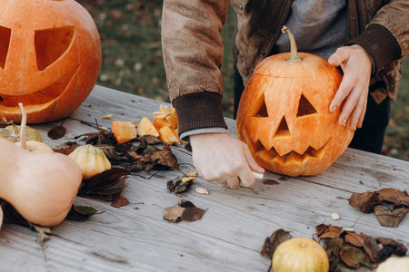 Man carving halloween pumpkin on rustic wooden table in autumn garden, hands close up. Fall harvest. Cutting pumpkin, making a jack o lantern. Halloween preparationの写真素材