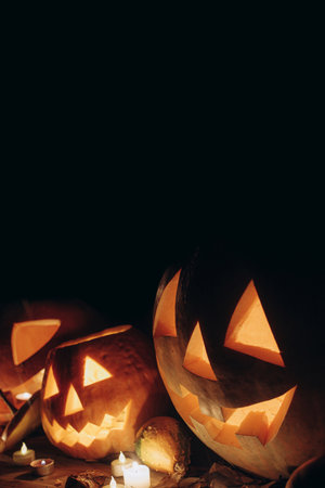Spooky glowing Jack o lanterns on rustic wooden table in dark autumn night. Scary atmospheric halloween carved pumpkins in evening garden. Boo! Trick or treat. Copy spaceの写真素材