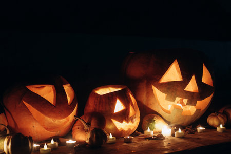 Spooky glowing Jack o lantern and candle light on rustic wooden table in dark autumn night. Scary...