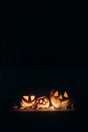 Jack o lantern glowing pumpkins with candles on rustic table in dark scary garden. Boo! Trick or treat! Spooky atmospheric Halloween night with space for textの写真素材