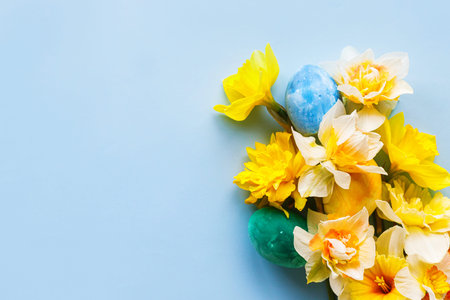 Easter flat lay. Stylish easter eggs and yellow daffodils flowers on blue background. Easter...