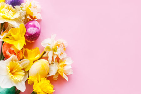 Happy Easter! Colorful Easter eggs with daffodils flowers flat lay on pink background. Stylish...