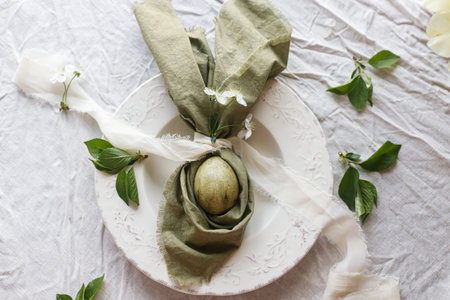 Happy Easter! Stylish dyed egg in bunny ears napkin and spring flowers  on plate. Easter celebration...
