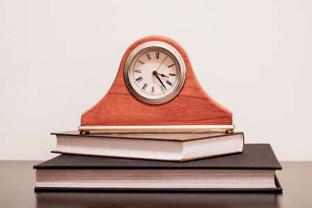 On the writing table are several books, and on the books are a clock with Roman numeralsの写真素材