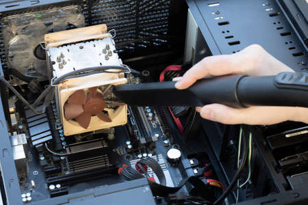 a very dirty computer fan inside the computer being cleaned with a vacuum cleaner close-upの写真素材