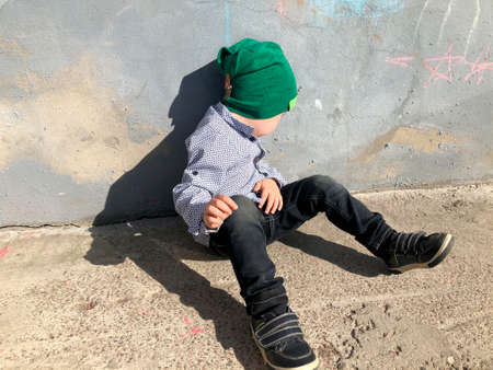 A disobedient child sits on the street near the wall and turns awayの写真素材