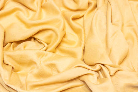 A beautiful womens accessory is a golden flowing scarf made of woolen thread. Yellow fabric texture from yarn.の写真素材
