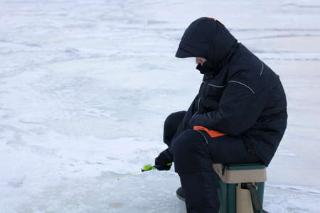The fisherman holds a fishing rod in his hands winter fishing, sits on the iceの写真素材