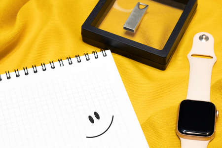 A notepad with a smiley face drawn on it and a smart watch with a flash drive. Modern new devices...