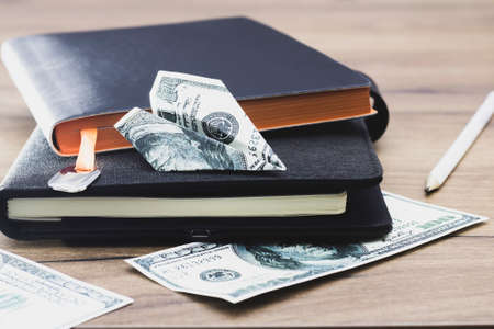 An airplane made of banknotes lies on a black stack of notepads on the table. The concept of financial growthの写真素材