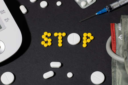 The word stop is lined with pills on the background of a syringe, drugs and a tonometer. The concept...