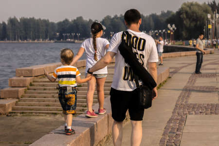 The family is walking in the park, dad, daughter and son 3 years old, athletes are running in the distance. Embankmentの写真素材