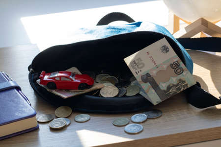Russian rubles and banknotes in a childrens bag on the table next to a toy car. Pocket money