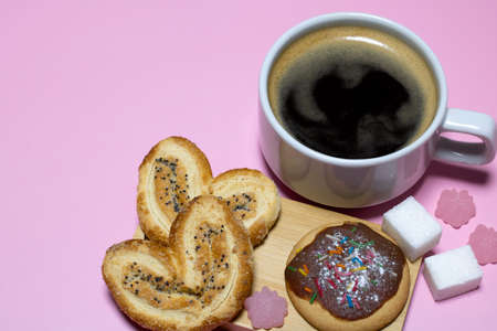 A cup of black coffee and cookies with marmalade candies on a pink background