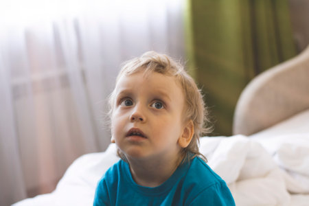 The morning rays of the sun from the window illuminate a blond-haired boy sitting thoughtfully on...