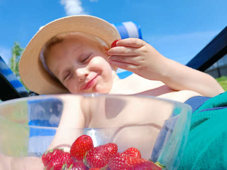 Strawberries in a glass bowl, a childs hand holds strawberries, a child eats strawberries, sunbathing in the sun.の写真素材