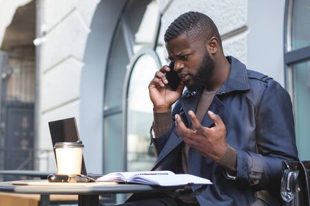 Angry african businessman talking on the phone at a cafe.の写真素材