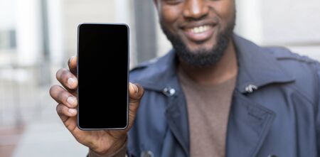Close up potrait of african man in autumn jacket holding a smart phone with screen for copy space.の写真素材