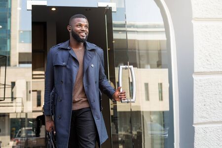 African millennial walking out of a building filled with joy, holding a black briefcase.の写真素材