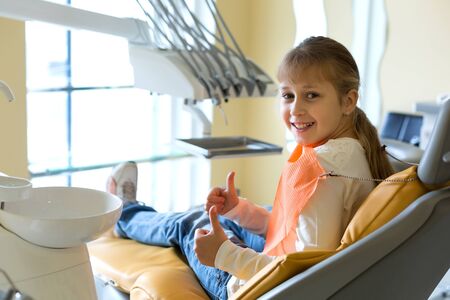 Small girl with a cute smile sitting on a dentist chair covering with a napkin waiting for a doctorの写真素材