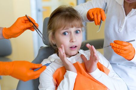 Scared little girl is afraid of dental tools for oral check-up held by dentistsの写真素材