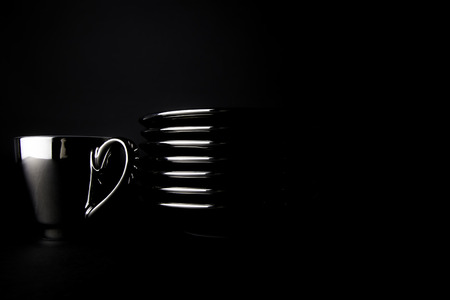 A single silver espresso cup by a stack of saucers isolated against a black background. The whole image is dark and luxurious reflecting the nature of a rich coffee.の写真素材