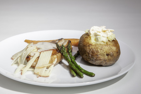 A baked potato with pork loin and shredded apple. Served with sauteed asparagus, carrots and chunky coleslaw.の写真素材