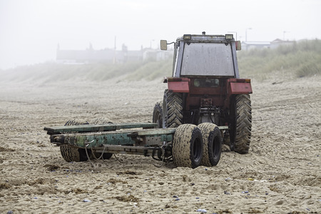 A red beach tractor with green trailer returning from launching a fishing boat on a misty morningの写真素材