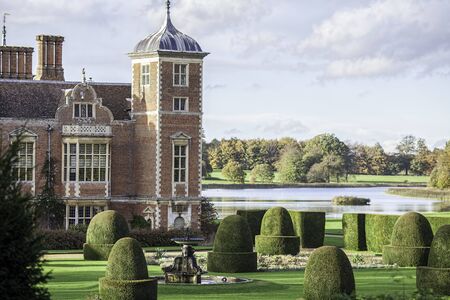 English country estate manor house with ornamental gardens and lake. Period details including dutch gable, topiary and water fountain. Rich gentry landscape.の写真素材