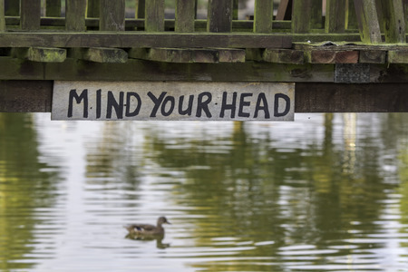 Mind Your Head. A quirky hand-written sign displayed below a low river bridge. の写真素材