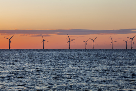 Offshore wind farm turbines caught in the orange glow of sunrise. Beautiful contrast with the blue sea. A great image to convey conservation via renewable energy sources.の写真素材