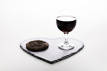 Romantic meal for one. A loving serving of chocolate and wine. Chocolate cookie and red wine on a heart-shaped slate coaster.の写真素材