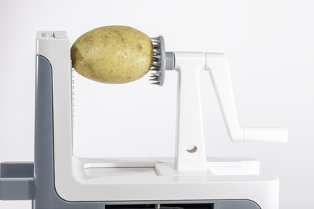 Potato in a vegetable spiralizer. Close-up against white background.の写真素材