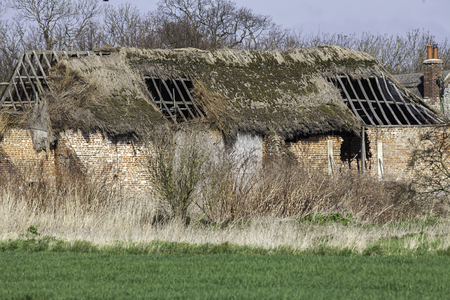 Dilapidated thatched roof barn conversion project. Derelict old red brick English barn with collapsed thatch roof. Ideal barn-conversion building property.の写真素材