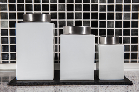 Square white storage jars in modern black and white tiled kitchen. Ceramic containers with label space.の写真素材