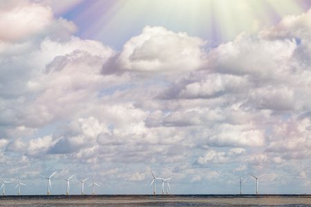 Save the Planet. Offshore wind farm on the horizon with sunlight breaking through cloud. Sustainable resources and clean energy. Sun light rays through a dense cloudscape at sea.の写真素材