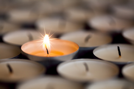 Selective focus on shining magical light of a single sparkling flame from one candle among many extinguished tealight candles. Christmas or celebration image of beautiful star flaming candlelightの写真素材