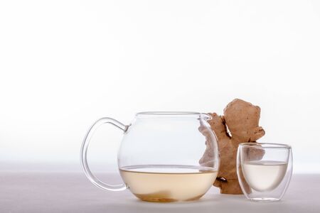 Ginger tea in teapot with glass and organic root. Healthy winter hot drink. Studio shot against...