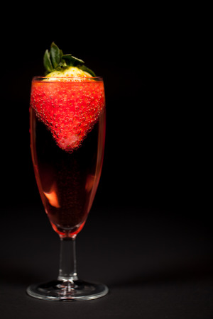 Celebration drink. Pink Champagne sparkling wine with strawberry. Rose bubbly alcoholic drink in glass against black background with copy space.の写真素材
