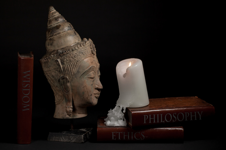 Philosophy ethics and wisdom. Buddhist enlightenment and religious education. Traditional buddha head statue with candle and philosophical text books. Meditation and spiritual awakening. の写真素材