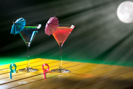 Holiday romance. Romantic vacation party cocktail drinks by moonlight. Pink and blue exotic moonlit beach cocktails representing his and hers fun and getaway decadence.の写真素材