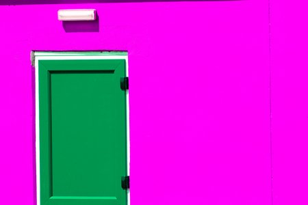 Vibrant colorful paint. Green painted door on striking neon pink building exterior. Bright colourful close-up image with dynamic colors.の写真素材