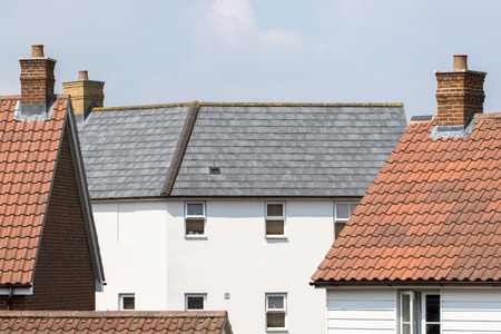 Contemporary suburban housing estate. Modern white house with slate roof tiles in between other homes.の写真素材